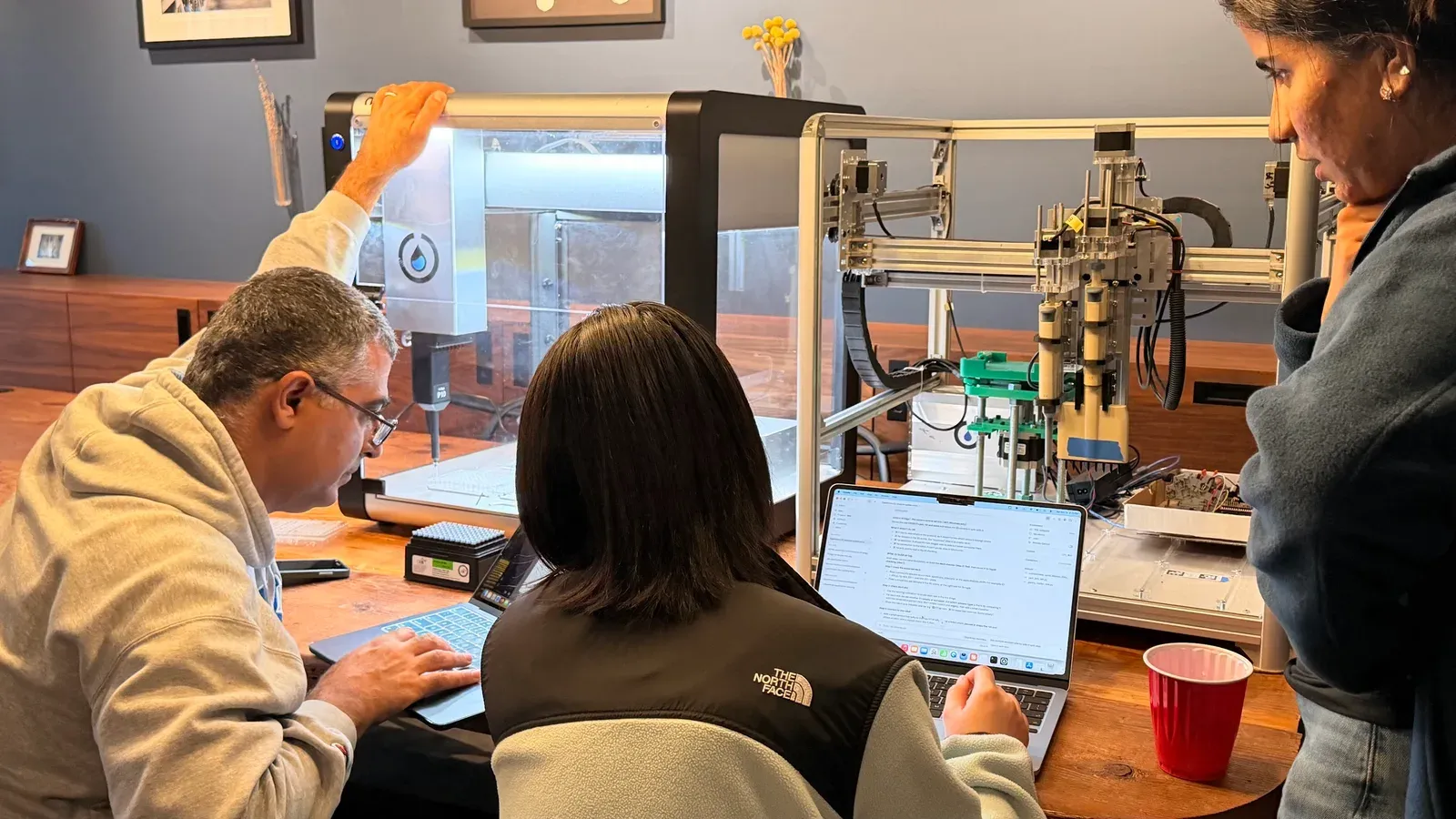 Builders collaborating around a laptop and benchtop lab automation equipment