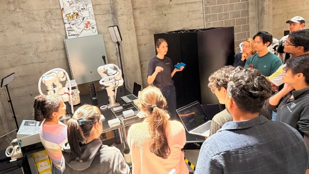 Builders gathered around robotic arms during the AI Science World Model Hack at Zeon Systems