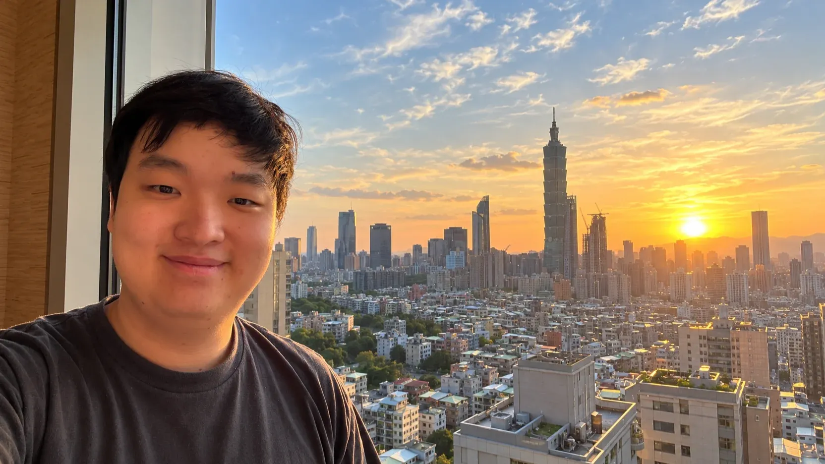 AI-edited portrait of Xiangan He beside a window overlooking Taipei 101 at sunset